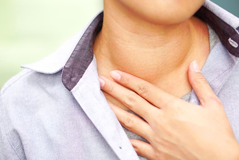 A patient with a goiter touches their neck