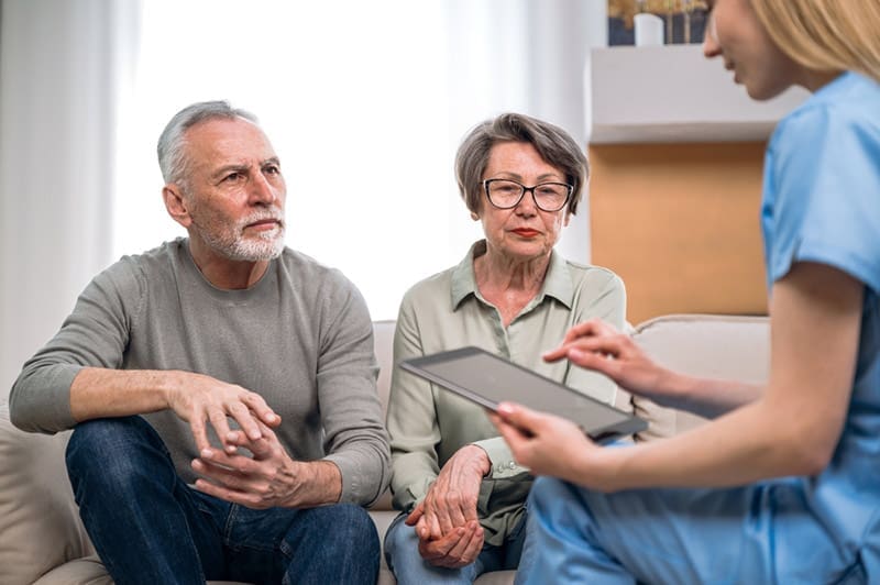 Two elderly patients consult with a clinician, who accesses insurance information on a tablet.